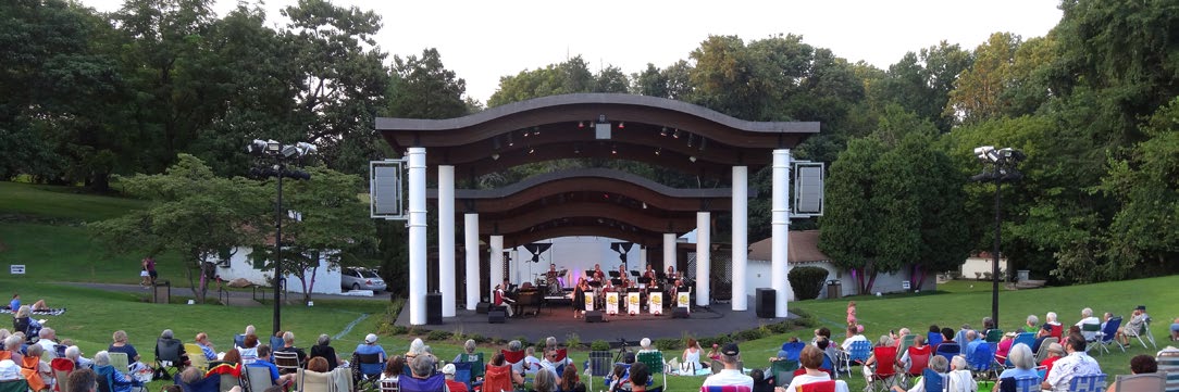 An audience on the lawn in front of the Rose Tree Park amphitheater during an evening concert
